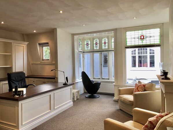 Une pièce spacieuse avec une grande fenêtre, un bureau avec une chaise, un canapé et un radiateur.