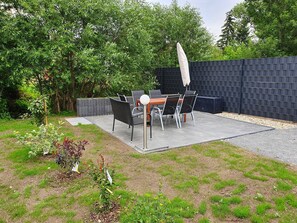 An outdoor patio with a table and chairs, surrounded by a black wall and greenery.
