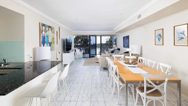 A modern kitchen with a granite countertop, white chairs, and a dining area with a wooden table and white chairs.