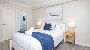 A neatly arranged bedroom with a bed, two bedside lamps, a wall-mounted artwork, and a small bedside table.