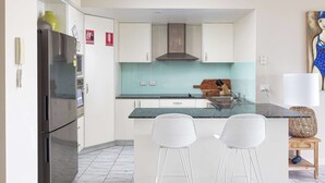 A modern kitchen with white cabinets, a stainless steel refrigerator, a built-in stove, and a large island with bar stools.
