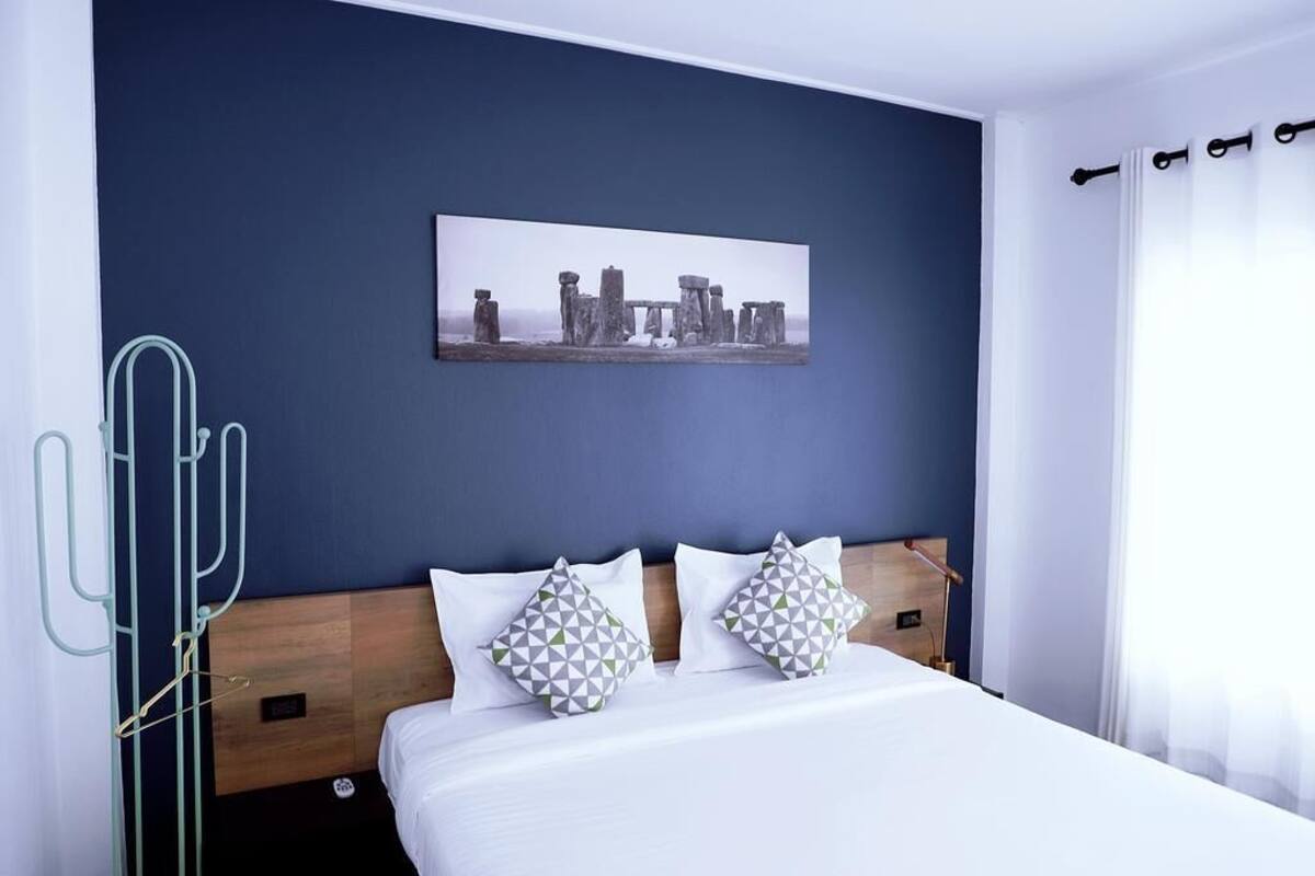 A hotel room with a bed, two pillows, a wall-mounted picture, and a nightstand.
