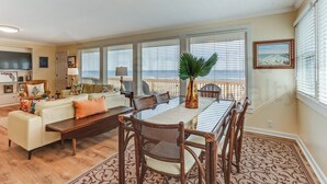 A spacious living room with a dining area, large windows, and a balcony. - South Fletcher Beachfront Home by RedAwning (Fernandina Beach)