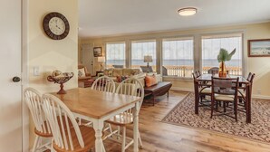 A dining area with a wooden table and white chairs, a clock on the wall, and a view of the ocean through large windows. - South Fletcher Beachfront Home by RedAwning (Fernandina Beach)