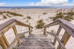 Een houten trap die naar een strand leidt, met duinen en een helder uitzicht op de oceaan.