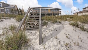 A beachfront property with a wooden staircase leading to a balcony, surrounded by sand and sparse vegetation. - South Fletcher Beachfront Home by RedAwning (Fernandina Beach)