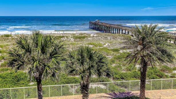 A beach with a wooden pier extending into the ocean, palm trees, and a fenced walkway. - Updated Condo Featuring Fresh Atlantic Breeze by RedAwning (Fernandina Beach)