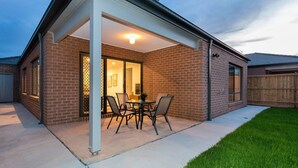A covered patio with a brick exterior, a glass door entrance, and a table with chairs. - Resortstyle 4BR House With Parking@werribee (Werribee)
