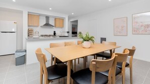 A modern kitchen with wooden cabinets, a central island, and a dining area with a wooden table and chairs. - Resortstyle 4BR House With Parking@werribee (Werribee)