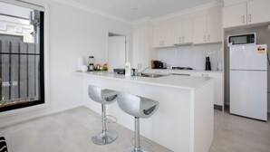 Une cuisine moderne avec des meubles blancs, un îlot central doté de tabourets, un four à micro-ondes et un réfrigérateur.