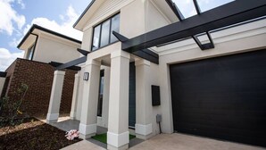 Une maison moderne à deux étages, dotée d’une porte de garage noire, de piliers blancs et d’un mur en briques.