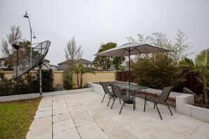 Une terrasse avec une table et des chaises en verre, un grand parasol et une antenne parabolique.