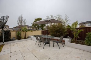 Une terrasse avec une table et des chaises en verre, un parasol et un jacuzzi.