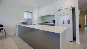 A modern kitchen with white cabinets, a large island, and a refrigerator with magnets. - Superb Luxe 5BR House@point Cook Near Lake (Point Cook)