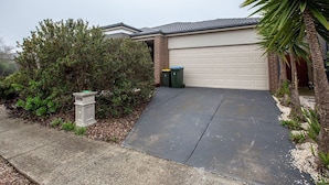 Garagem residencial com fachada de tijolos, calçada de concreto e um pequeno jardim com arbustos e uma palmeira.