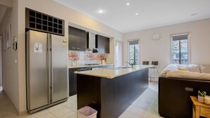 Cozinha moderna com ilha central, eletrodomésticos de aço inoxidável e área de refeições com sofá e mesa.