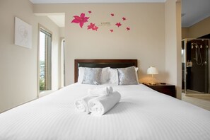 A hotel room with a large bed, a nightstand with a lamp, a shower area, and a wall with a floral decal. - Gorgeous 4BR Home in Point Cook (Point Cook)