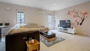 Uma sala de estar moderna com sofá, mesa de centro, televisão e arte decorativa na parede.