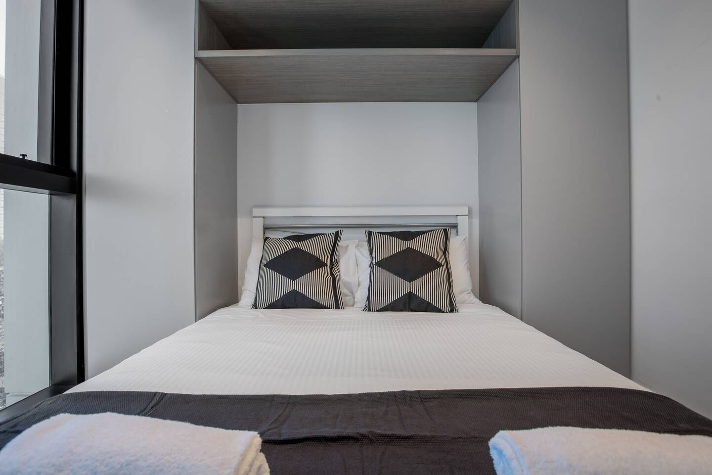 A small, modern bedroom with a bed, two pillows, and a window.
