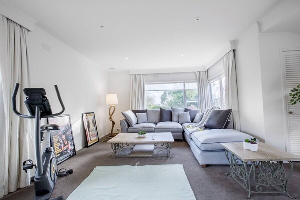 A modern living room with a grey sofa, a coffee table, a standing exercise bike, and a lamp.