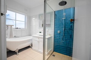 A modern bathroom with a freestanding bathtub, a glass-enclosed shower, and a window providing natural light.