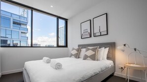 A modern hotel room with a large bed, a nightstand, a desk lamp, and two framed pictures on the wall. - Cozy APT Seaview Next to Southern Cross/pool/gym (Melbourne)