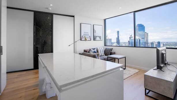 A modern living room with a large window, a sofa, a coffee table, and a TV. - Cozy APT Seaview Next to Southern Cross/pool/gym (Melbourne)