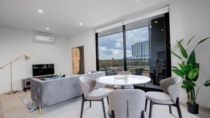 A modern living room with a sofa, a TV, a round dining table, and chairs. - Designer 2BR With Carpark Monash Uni@caulfield (Caulfield North)