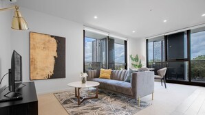 A modern living room with a grey sofa, a round coffee table, and a large abstract painting on the wall. - Designer 2BR With Carpark Monash Uni@caulfield (Caulfield North)