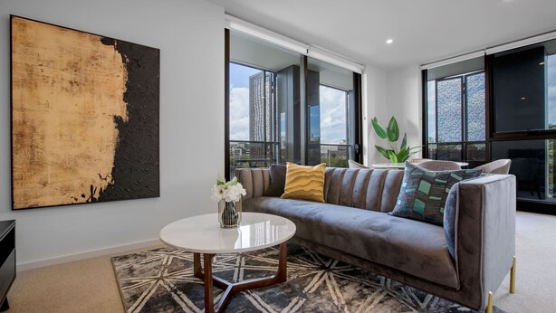 A modern living room with a gray sofa, a round coffee table, and a large abstract painting on the wall. - Designer 2BR With Carpark Monash Uni@caulfield (Caulfield North)