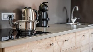 Een keuken met een roestvrijstalen pan op een inductiekookplaat, een zwarte koffiezetapparaat en een gootsteen met een kraan.