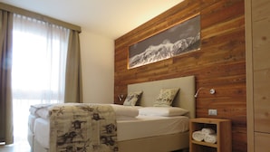 Een slaapkamer met een houten hoofdbord, een bed met een geborduurd plaid, twee kussens, een nachtkastje met een opgevouwen handdoek, en een ingelijst foto aan de muur.