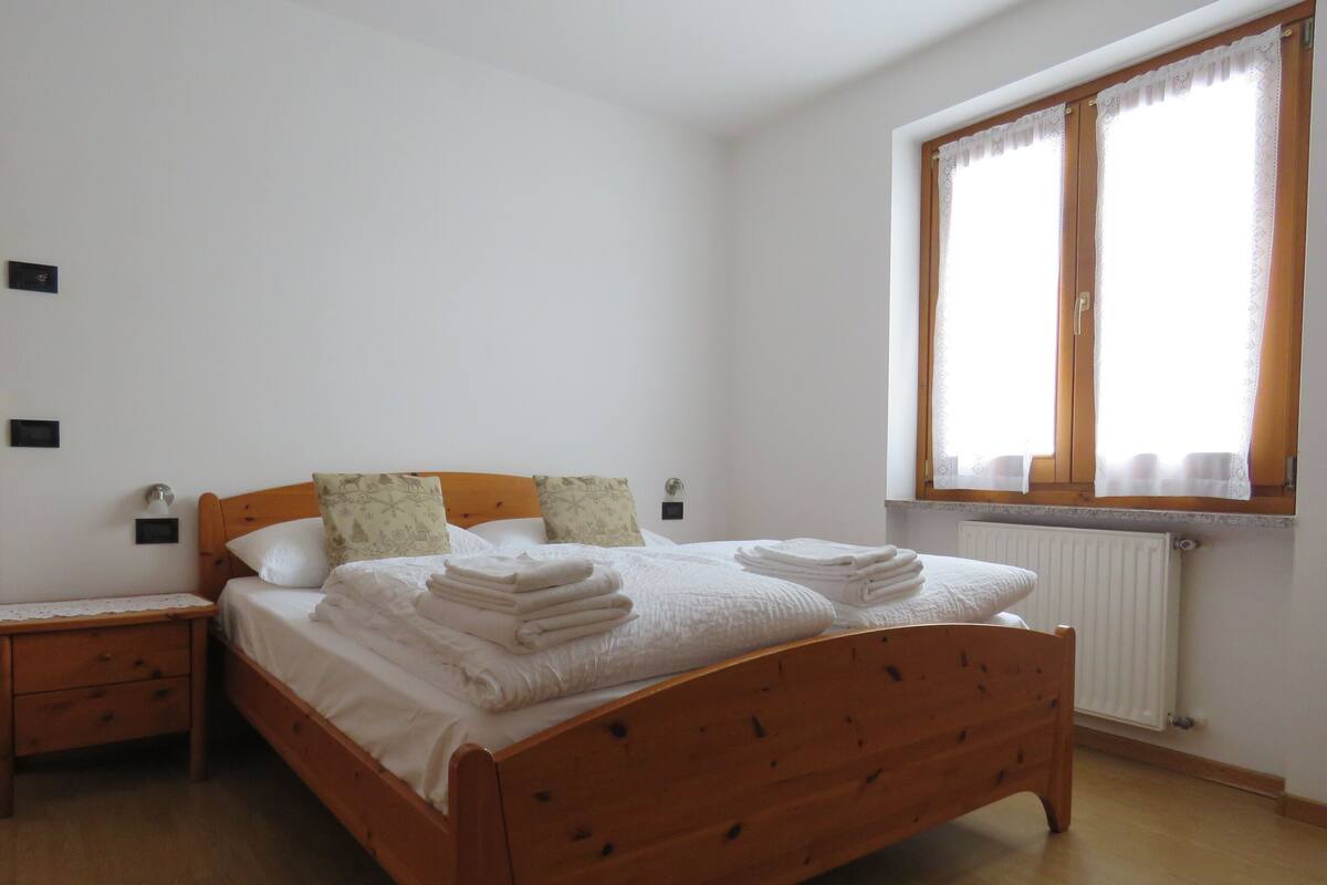 A bedroom with a wooden bed, white linens, two bedside tables, and a window with curtains.