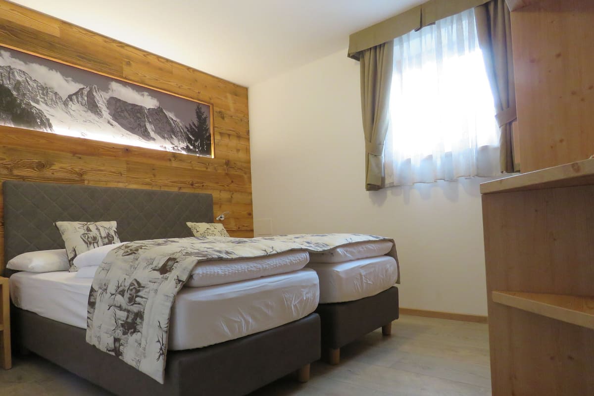A bedroom with a wooden headboard, two beds, a nightstand, and a wooden wardrobe.