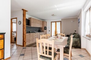 Un coin repas avec une table et des chaises en bois, une cuisine à l’arrière-plan et un canapé dans un coin.