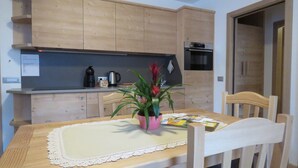 Een houten eettafel met een kantoonlap, omringd door houten stoelen. Op de tafel staat een potplant met rode bloemen.