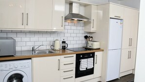 A compact kitchen with white cabinets, a stainless steel range hood, a built-in dishwasher, a coffee maker, and a toaster.