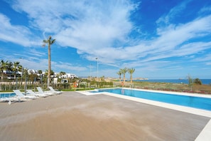 A pool area with lounge chairs, palm trees, and a view of the ocean. - Apartamento Rosa Chenz (Mar de Pulpi) (San Juan de los Terreros)