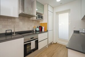 A modern kitchen with white cabinets, a stainless steel range hood, a microwave, and a wooden cutting board.