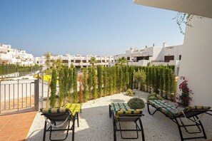 Une terrasse avec des sièges extérieurs, une vue sur des bâtiments blancs et un chemin de gravier.
