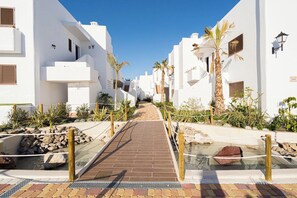 A pathway leading through a white building complex with palm trees and a small water feature.