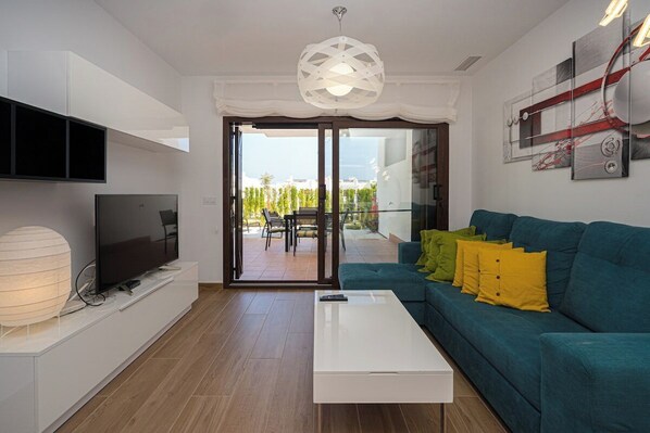 A modern living room with a flat-screen TV, a white coffee table, and a teal sofa with yellow cushions. - Apartamento Rosa Chenz (Mar de Pulpi) (San Juan de los Terreros)