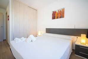 A hotel room with a bed, a nightstand with a lamp, a painting on the wall, and a door to another room.