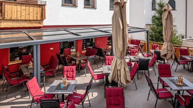 Een terras met rode stoelen en tafels, een klokkentoren en een gebouw met een bord waarop staat 