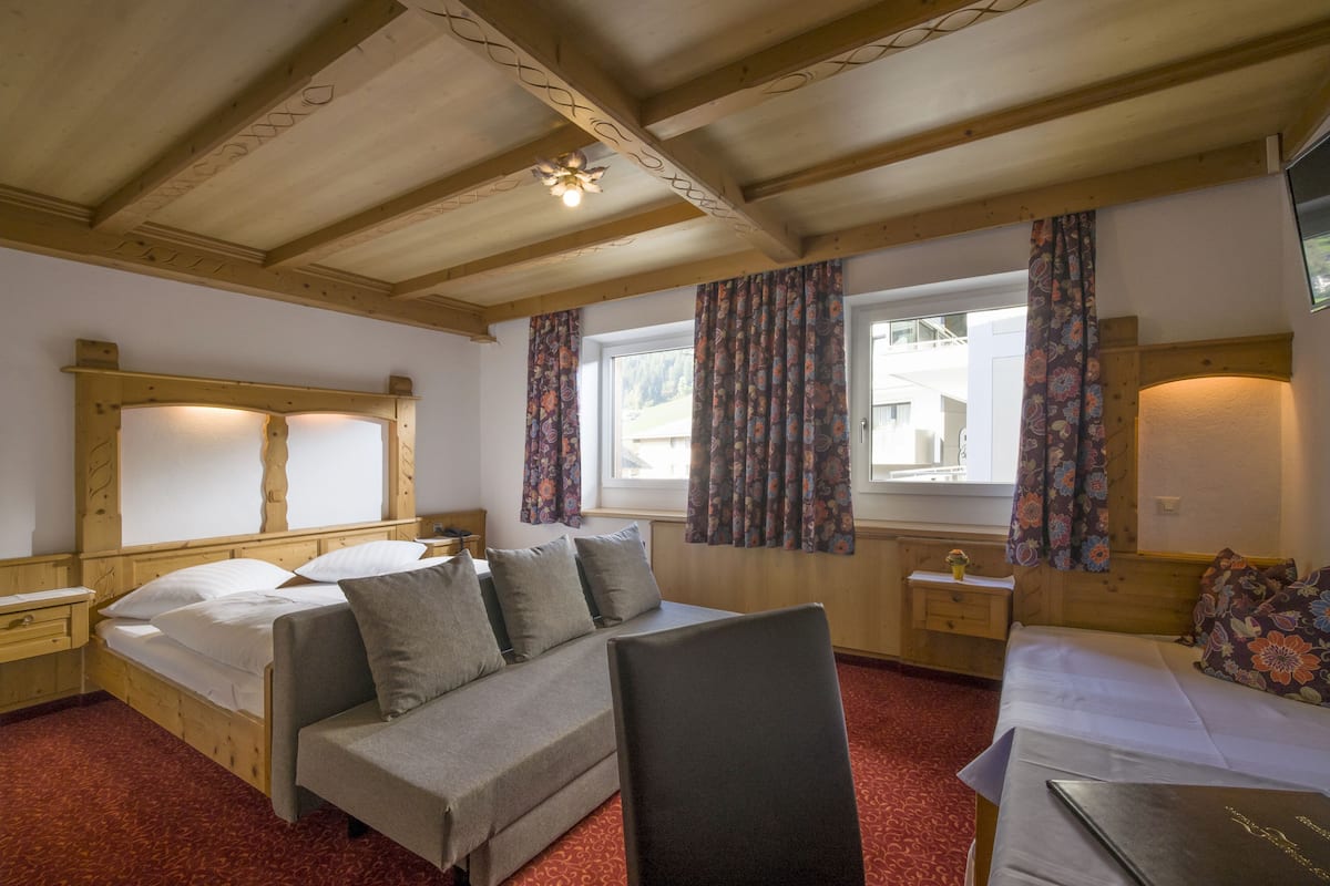 Ein Hotelzimmer mit Holzboden, zwei Betten mit blumigen Vorhängen, einem Holzkopfstück und einem kleinen Nachttisch mit Lampe, sowie einem roten Teppichboden.