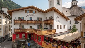 Een hotel met een opvallende kerktoren, een rood-witte gevel, en terrasstoelen met parasols.