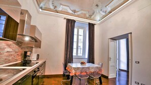 Cocina moderna con estufa integrada, microondas y campana extractora de acero inoxidable. Hay una mesa de comedor con sillas y una ventana con cortinas.