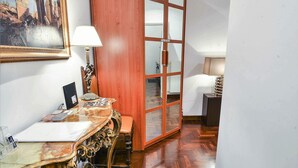 Un pasillo con suelo de madera, un escritorio con lámpara, un cuadro enmarcado y un armario de madera.