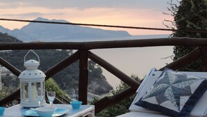 Een balkon met een tafel gedekt voor twee personen, een witte lantaarn en uitzicht op zee en bergen.