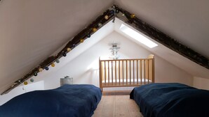 Une petite chambre mansardée avec deux lits, un plancher en bois, un plafond en pente et un puits de lumière.